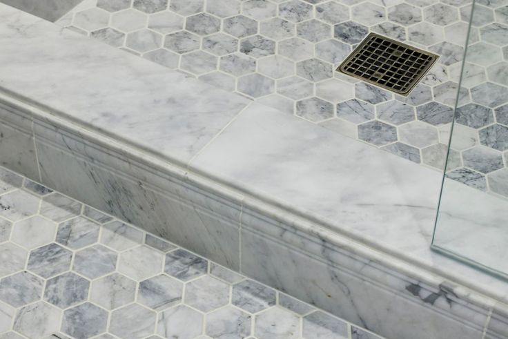 a bathroom with marble tile and hexagonal floor tiles on the shower wall, along with a metal grate in the middle