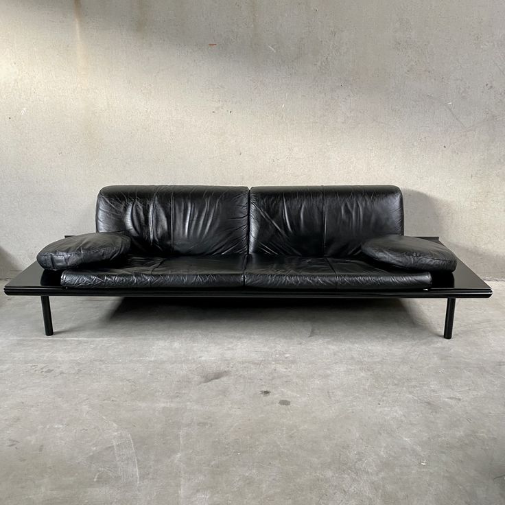 a black leather couch sitting on top of a cement floor next to a white wall