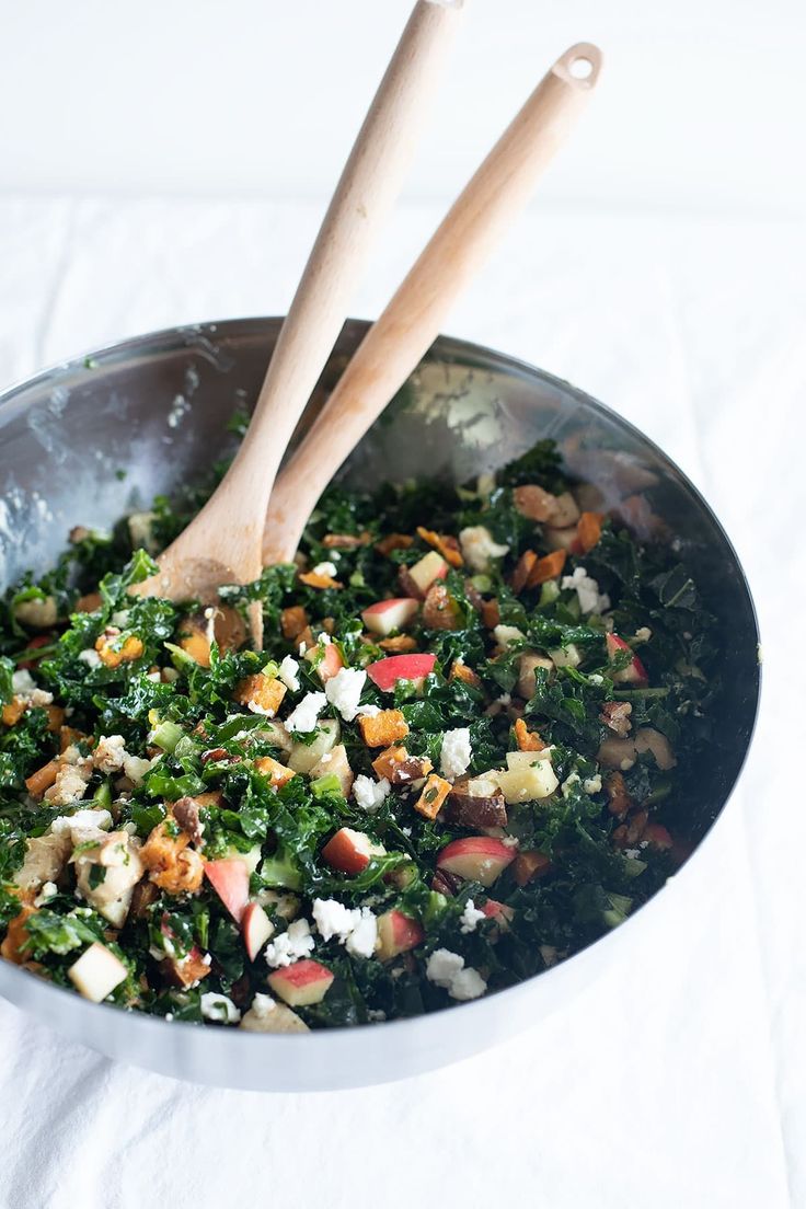 two wooden utensils in a bowl filled with kale and apple salad