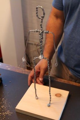 a man is working on a sculpture made out of wood and metal wire, with one hand holding the base