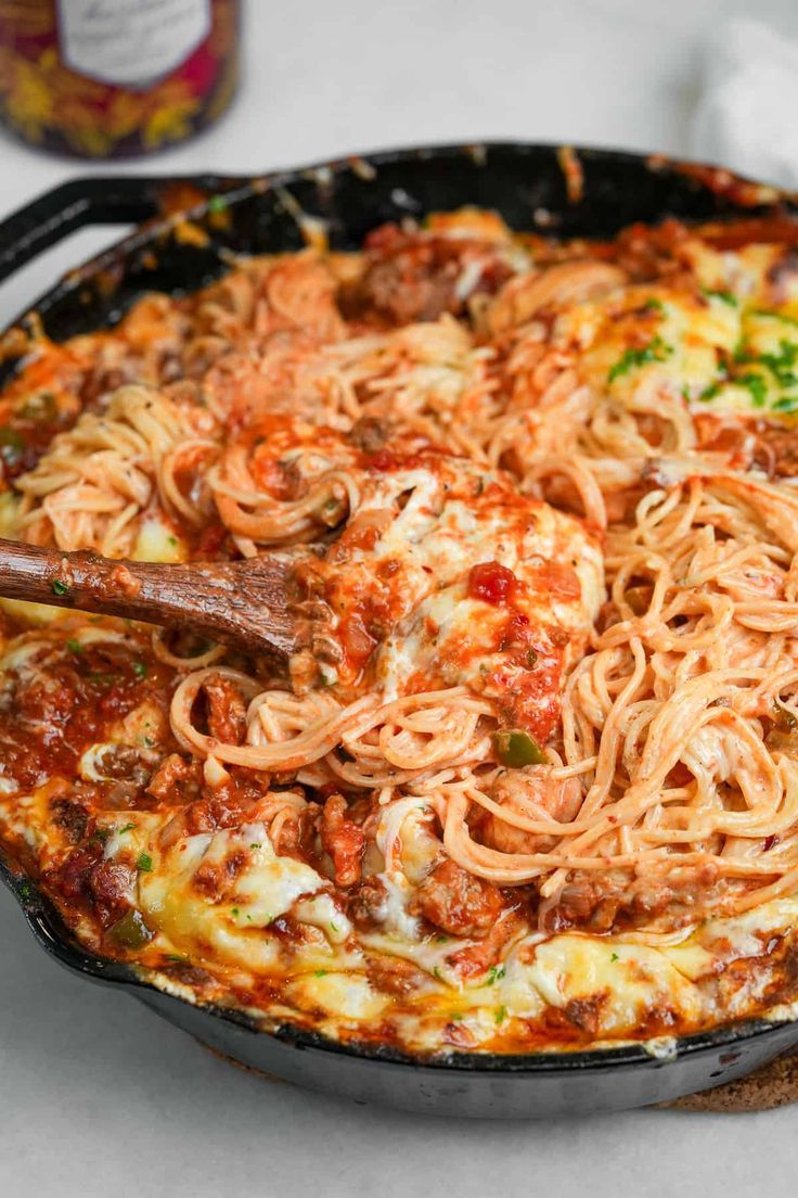 a skillet filled with pasta and sauce on top of a table next to bread