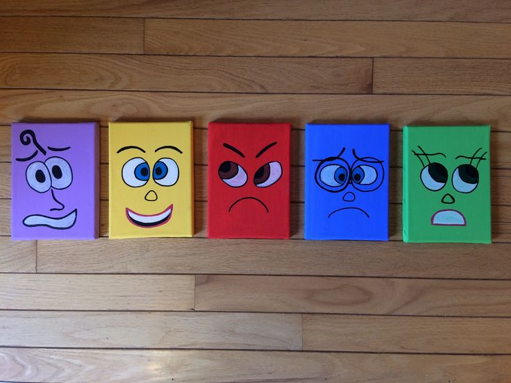 four blocks with faces painted on them sitting on a wooden floor next to a wall