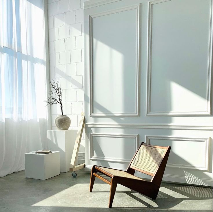 a chair sitting in front of a window next to a vase with a tree on it