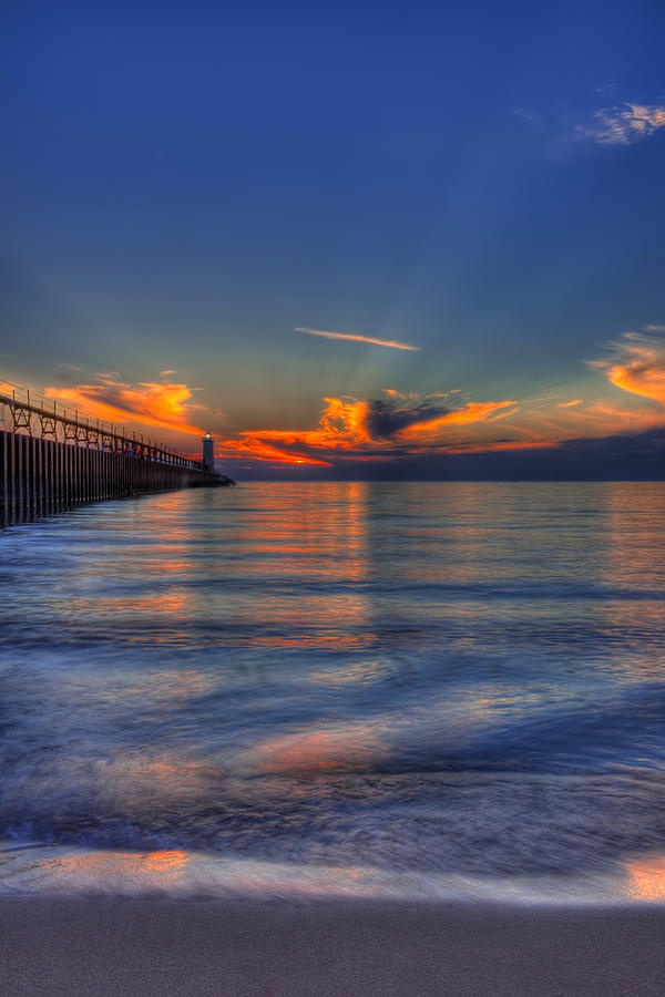 the sun is setting over the ocean with a pier in the foreground and clouds in the background