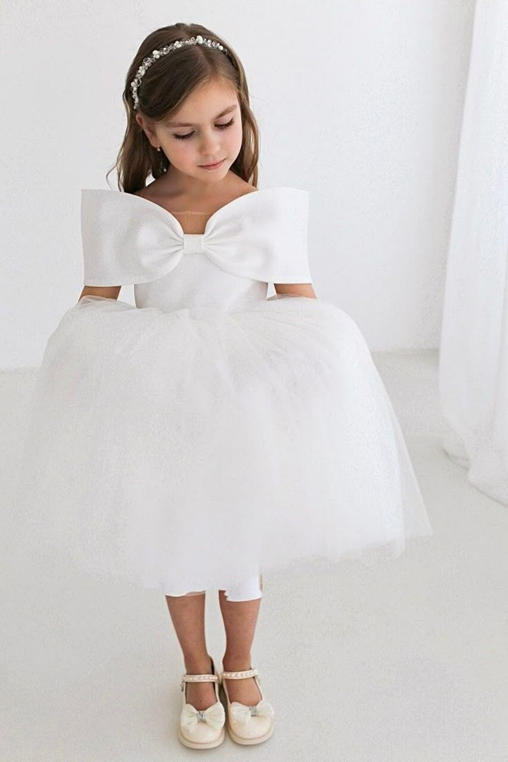 A charming white flower girl dress with a gorgeous puffy tutu skirt and a big bow for a truly royal look.  The dress features a sweetheart neckline, off shoulder sleeves, and a skirt layers of soft tulle.  The bodice has a sheer mesh to hold dress on shoulders so it doesn't slip down or roll up. It's easy to put on and take off, comfortable to wear and easy move. The dress has a zip at the back and 100% cotton lining for safe wear. The dress comes in pure white satin shining (it has a lurex thre Princess Dress Long, Toddler Wedding Dress, Long Tulle Dress, Dress With Big Bow, Party Short Dress, Skirt Layers, Communion Wedding, White Flower Girl Dress, Puffy Dress