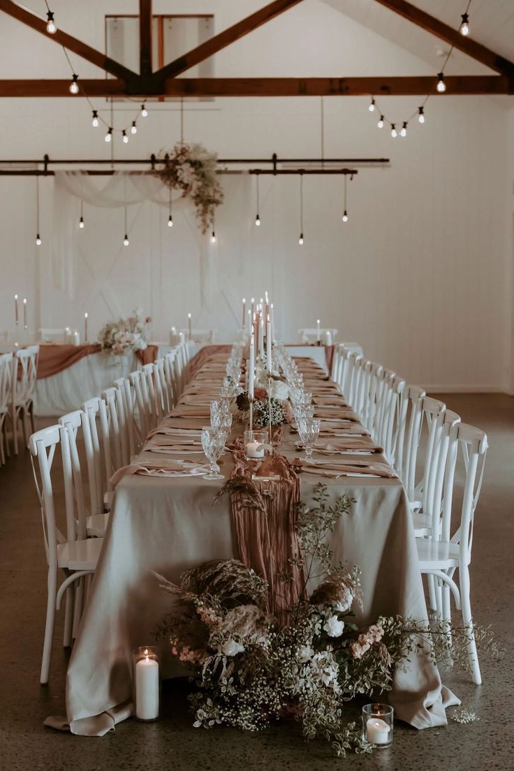 a long table is set up with white chairs and candles for an elegant wedding reception