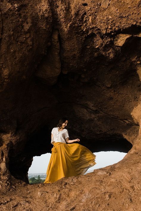 a woman in a long yellow skirt is standing near a cave