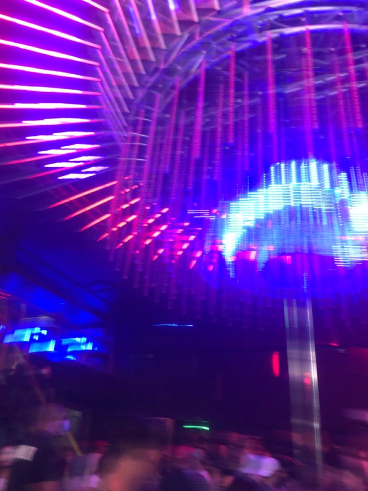 blurry image of people in a bar with neon lights on the ceiling above them