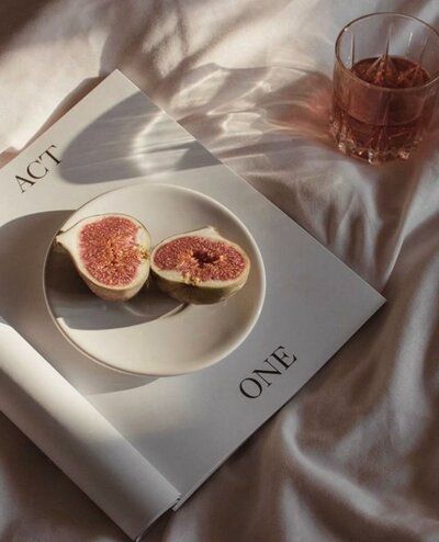 an open book with two figs on it next to a glass of wine and a drink