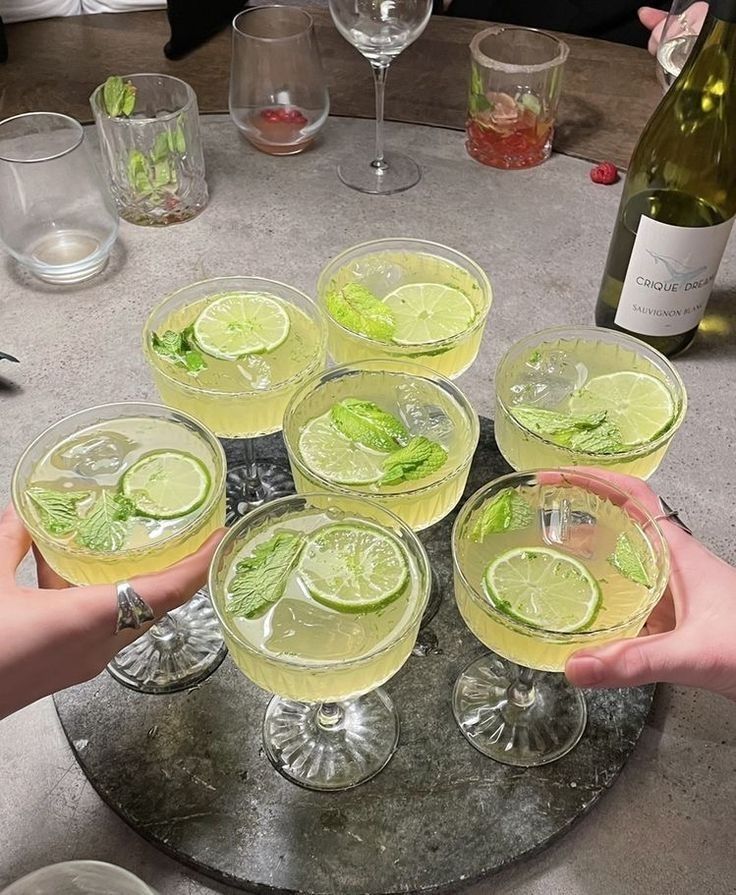 several people holding up glasses filled with different types of drinks on a table next to wine bottles and glasses