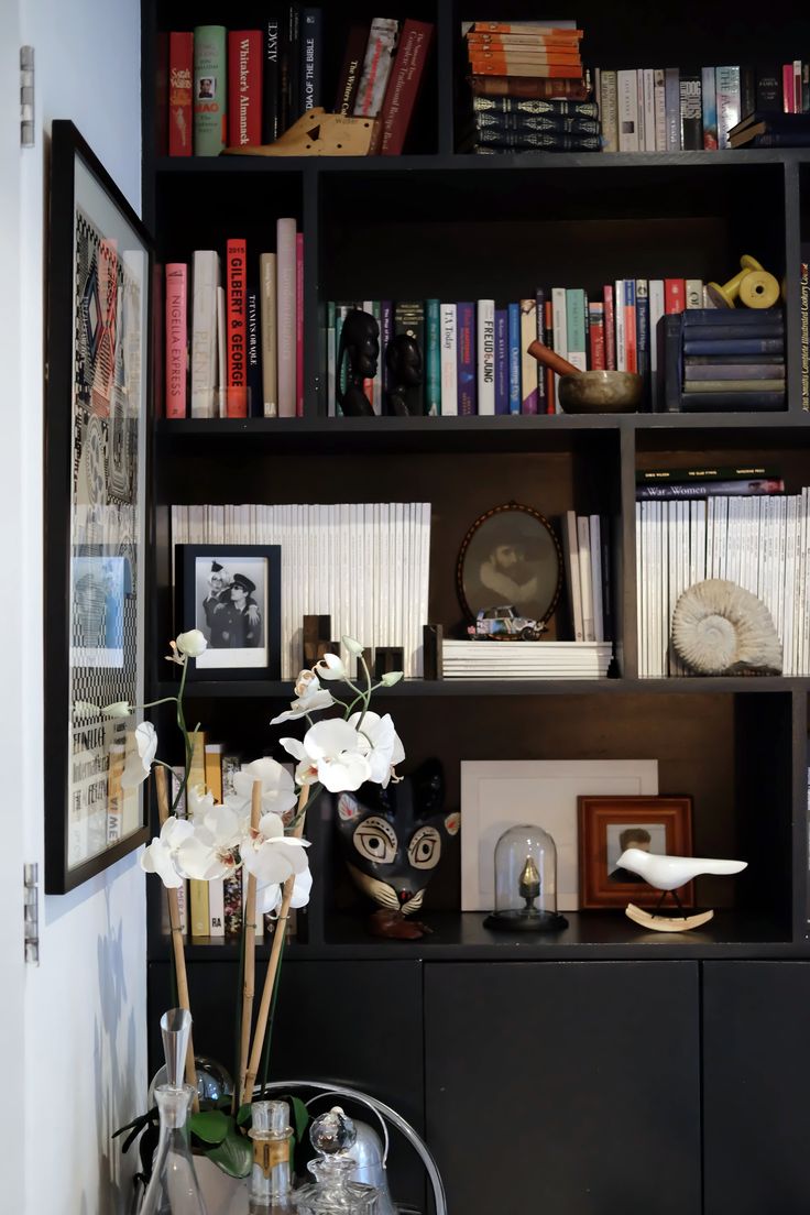 a black bookcase filled with lots of books next to a vase full of flowers