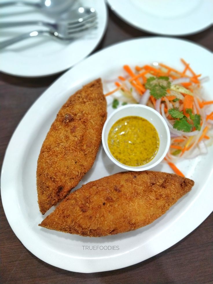 two fish fillets on a white plate next to a salad and dipping sauce in a small bowl