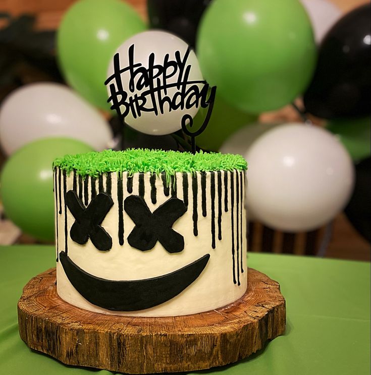 a happy birthday cake with green frosting and black icing, on top of a tree stump