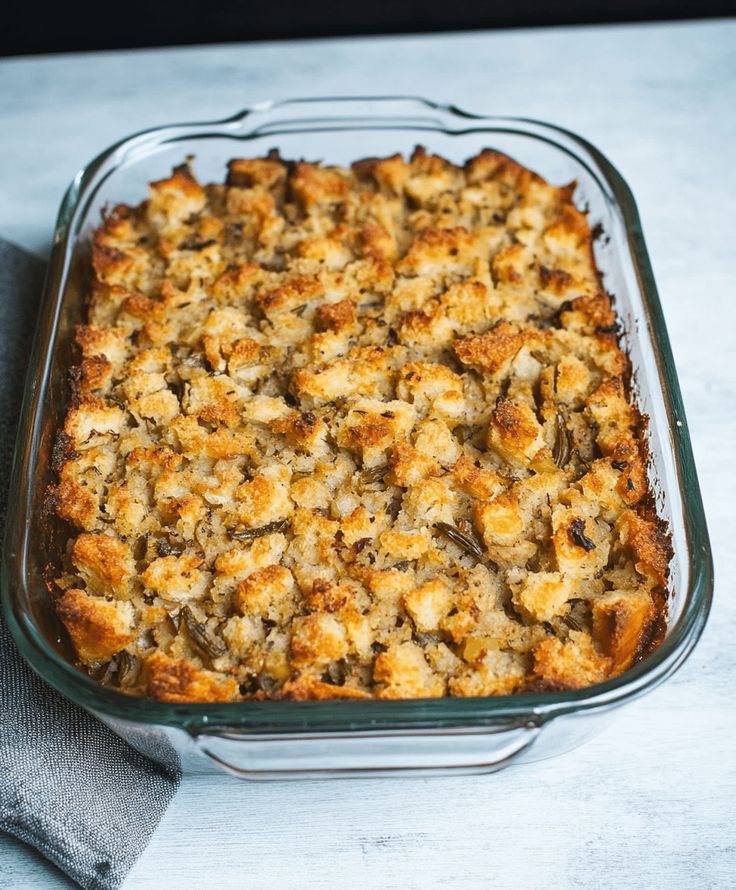 a casserole dish filled with stuffing on top of a white tablecloth next to a gray napkin