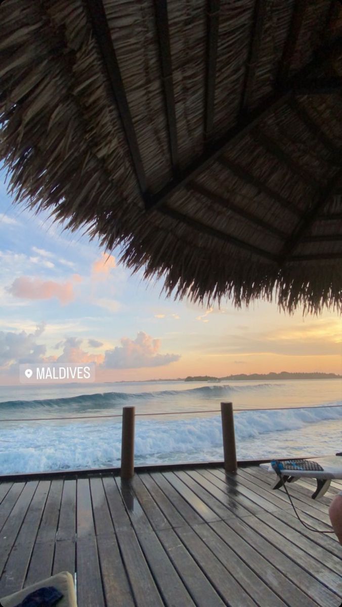 the sun is setting over the ocean with chairs and umbrellas