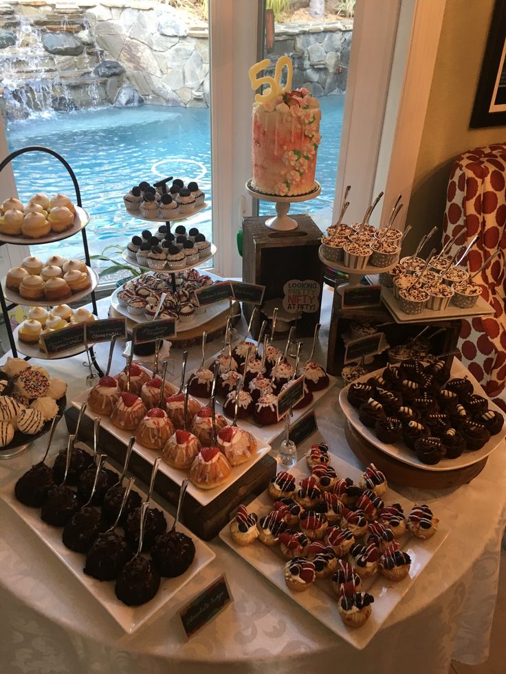 a table topped with lots of desserts next to a window filled with blue water