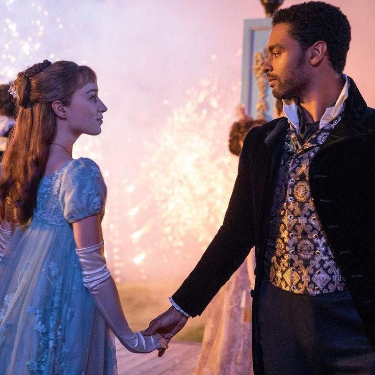 a man and woman holding hands while standing next to each other in front of fireworks