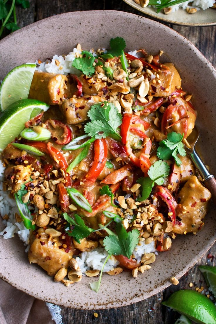 a bowl filled with rice and vegetables on top of a wooden table next to lime wedges