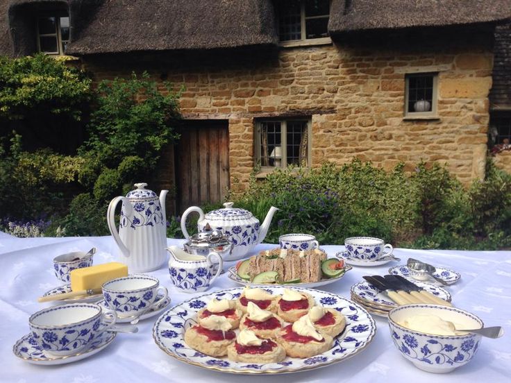 a table topped with plates and cups filled with food next to a stone building covered in thatched roofing