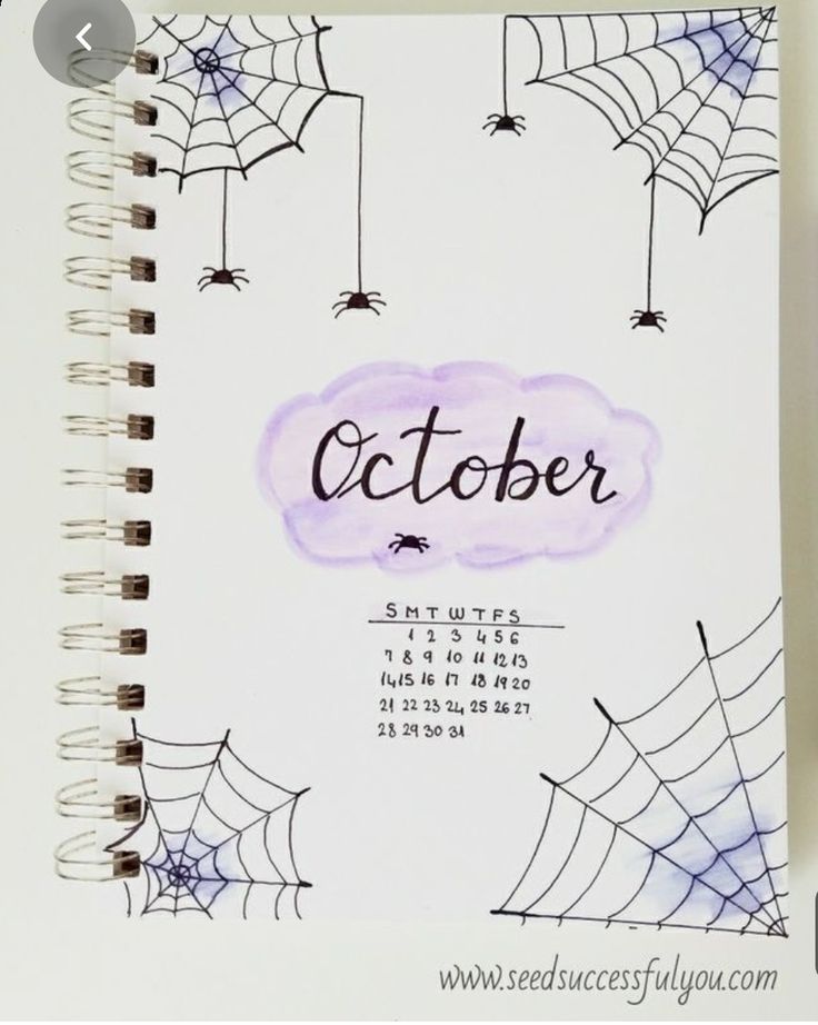 a spiral notebook with the word october written on it and spider webs hanging from strings