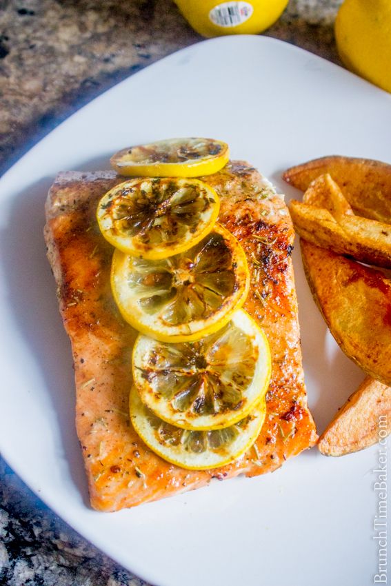 a white plate topped with fish, chips and lemon wedges next to a glass of orange juice