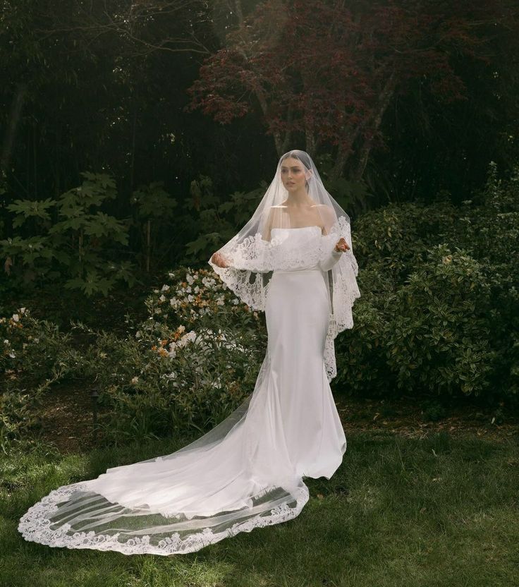 a woman in a white wedding dress and veil posing for the camera with her hands on her hips