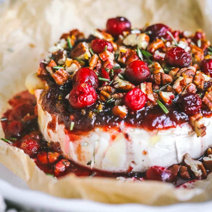 a piece of cheese covered in cherries on top of parchment paper with nuts and cranberry sauce