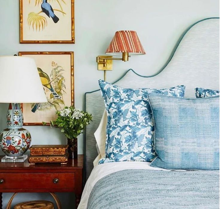 a bedroom with blue and white bedding, two pictures on the wall and a lamp