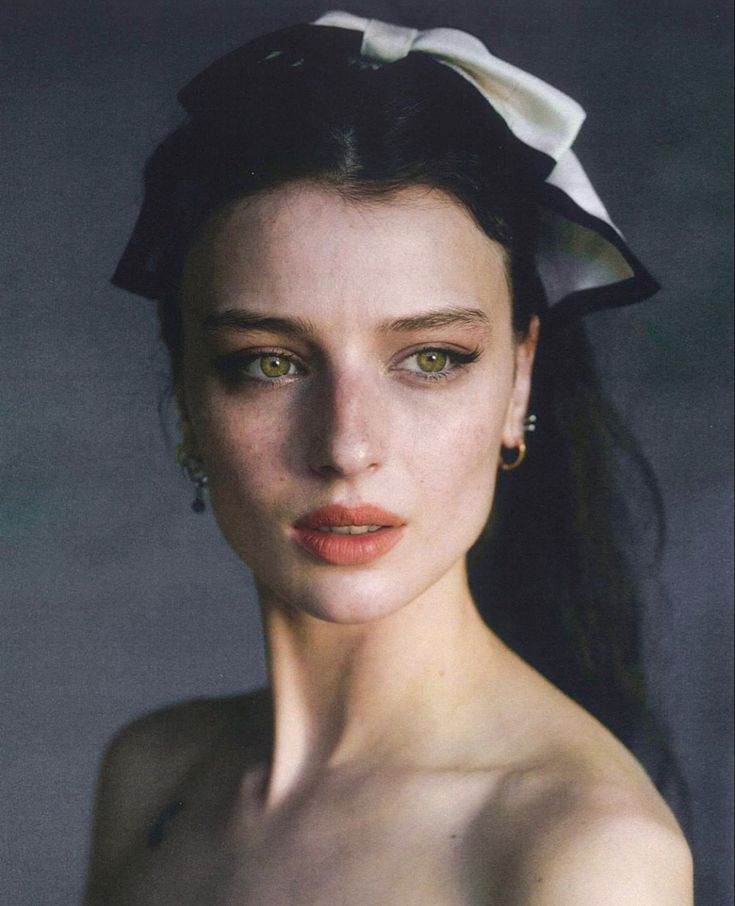 a woman with long black hair wearing a white flower in her hair and green eyes