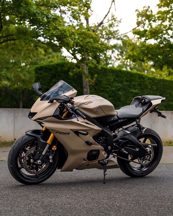 a tan motorcycle parked on the street next to some trees