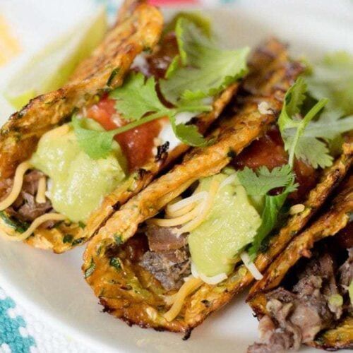 three tacos on a plate with lettuce, tomatoes and other toppings