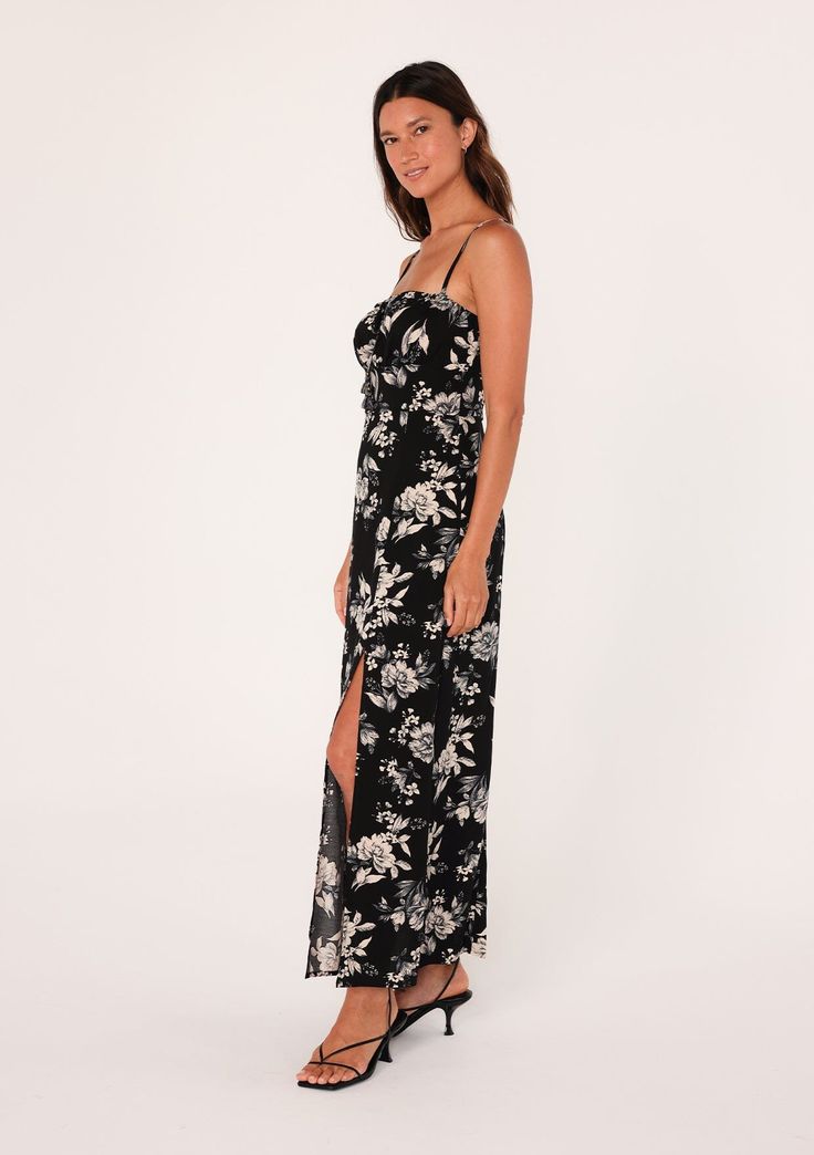 [Color: Black/Natural] A side facing image of a brunette model wearing a special occasion boho maxi dress in a black and off white floral print. With adjustable spaghetti straps Flowy Sleeveless Dresses With Side Slits, Floral Print Maxi Sundress For Date Night, Sleeveless Floral Maxi Dress For Date Night, Sleeveless Printed Maxi Dress For Date Night, Black Maxi Dress With Side Slits For Vacation, Casual Maxi Dress With Floral Print And Split, Casual Printed Maxi Dress For Date Night, Black Spring Maxi Dress With Split, Chic Floral Print Maxi Dress With Split