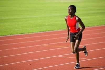 a woman running on a track in a red shirt and black shorts with her hands behind her back