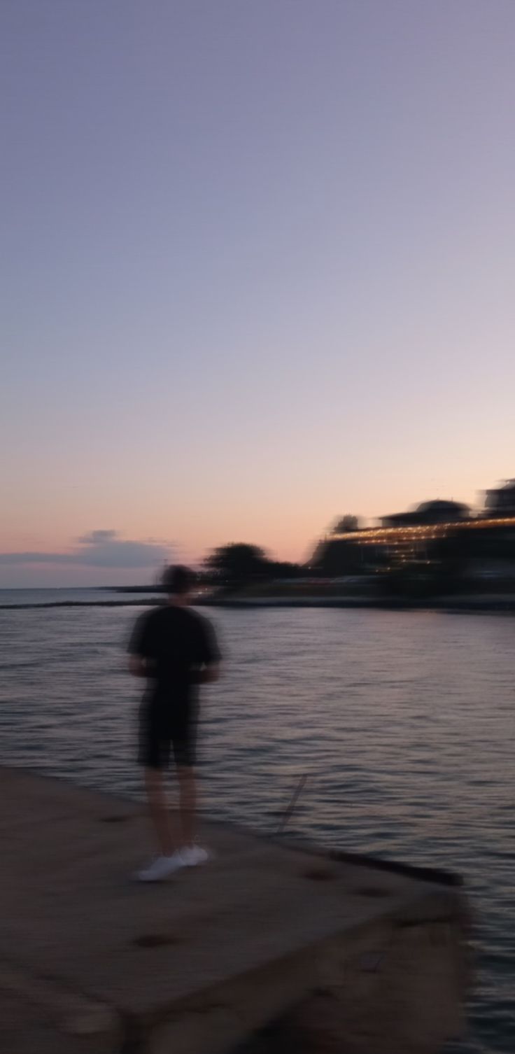 a person standing on a dock in the water at sunset or dawn with an airplane flying overhead