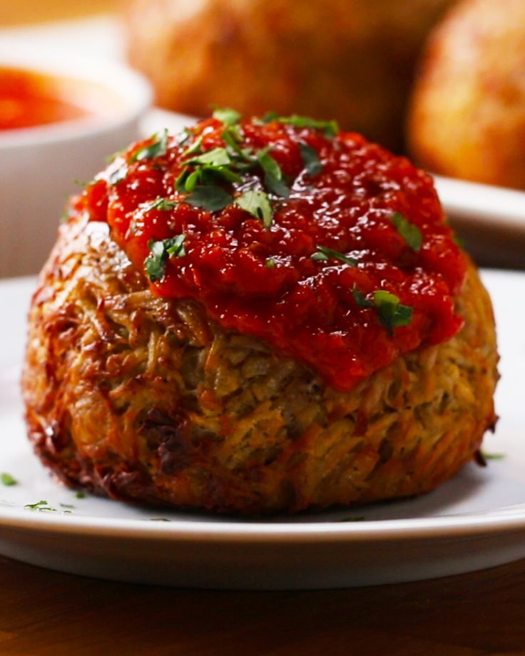 a meatball covered in marinara sauce on a white plate with other food items