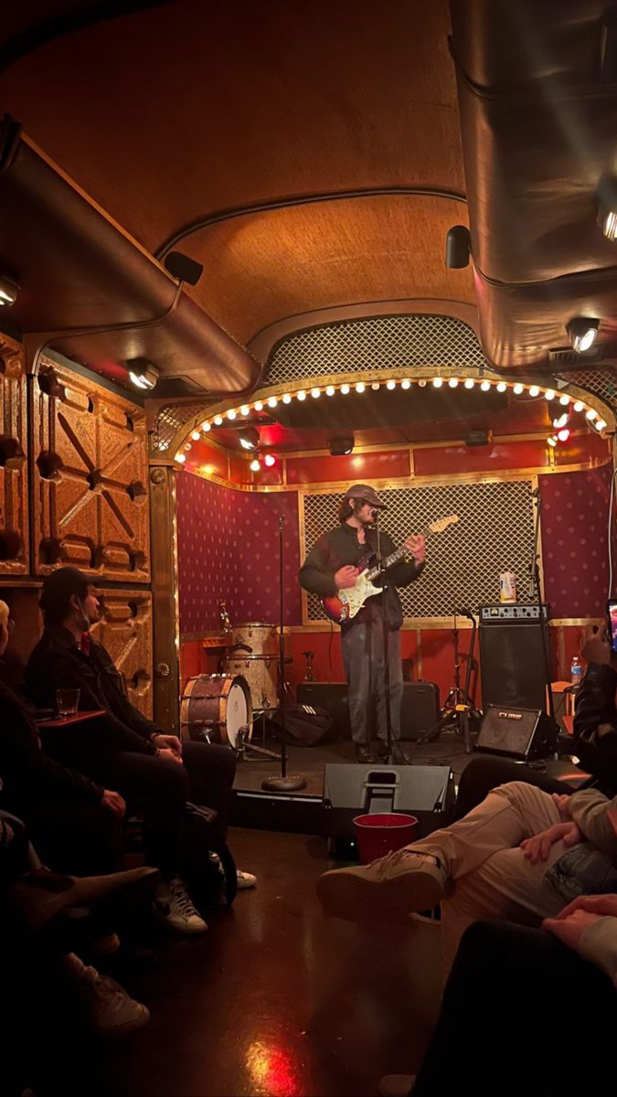 a group of people sitting in front of a stage playing guitars and singing into microphones