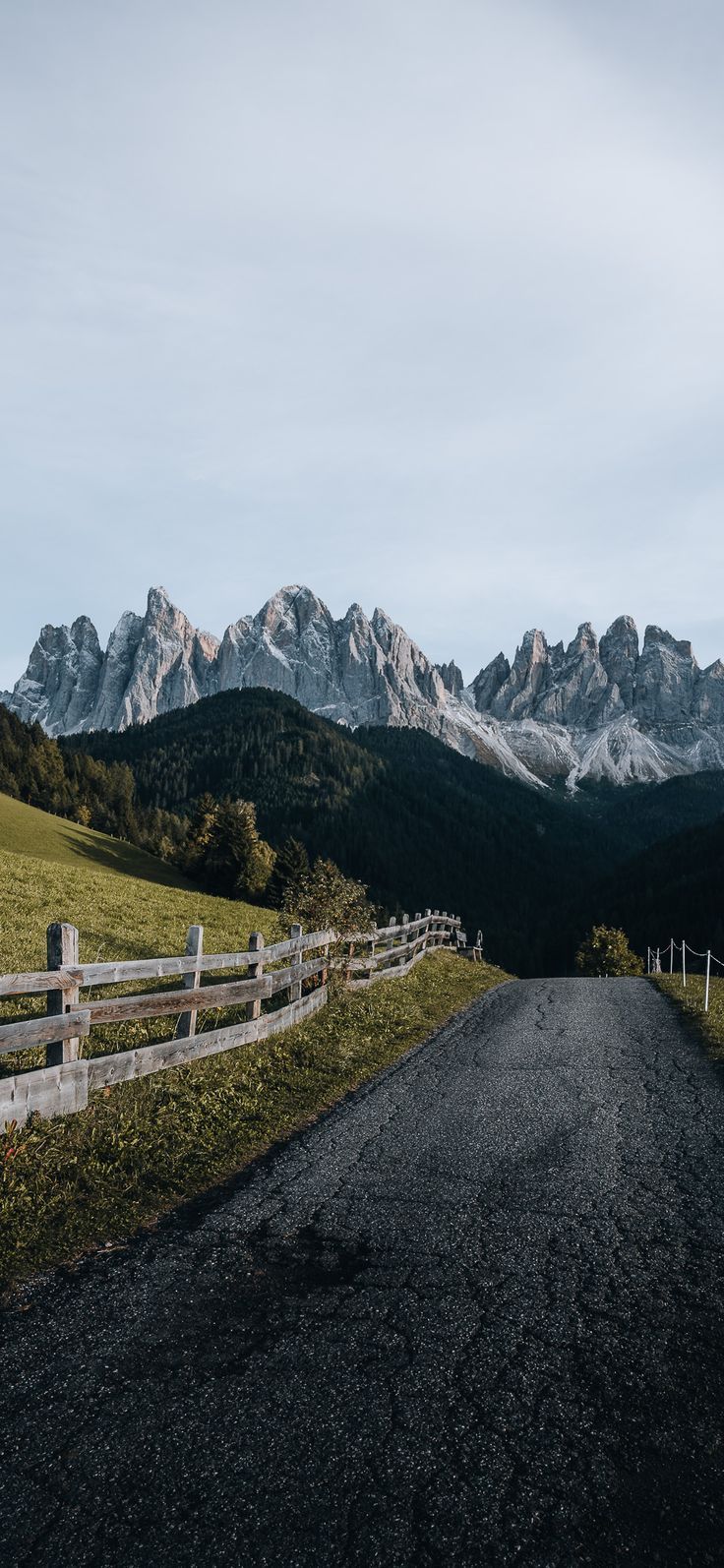 a dirt road in front of mountains with a wooden fence