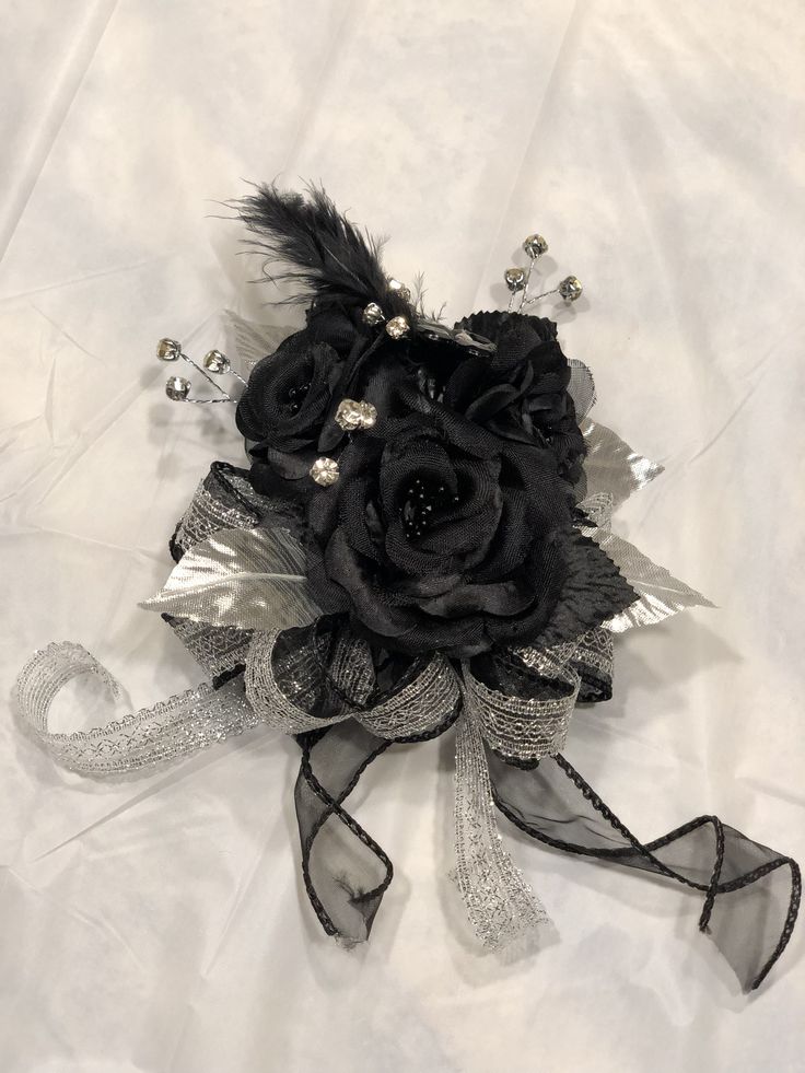 a black rose and feathers corsage on a white cloth with sequins