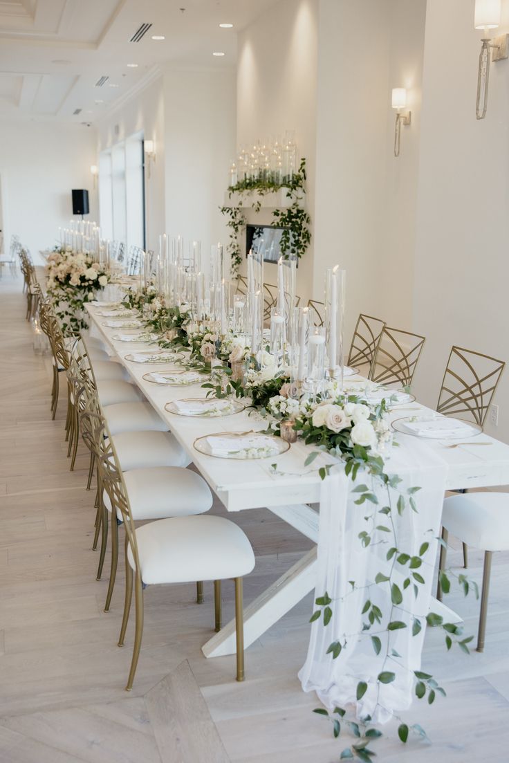 the long table is set with white flowers and greenery for an elegant wedding reception