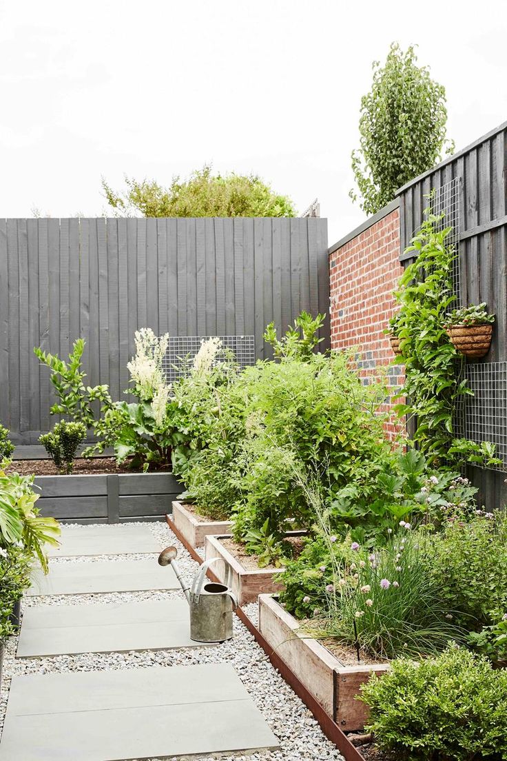 a garden with lots of plants and rocks in the ground, along side a fence