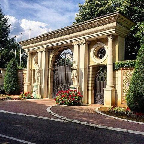 an arch in the middle of a road with flowers growing on it and trees around