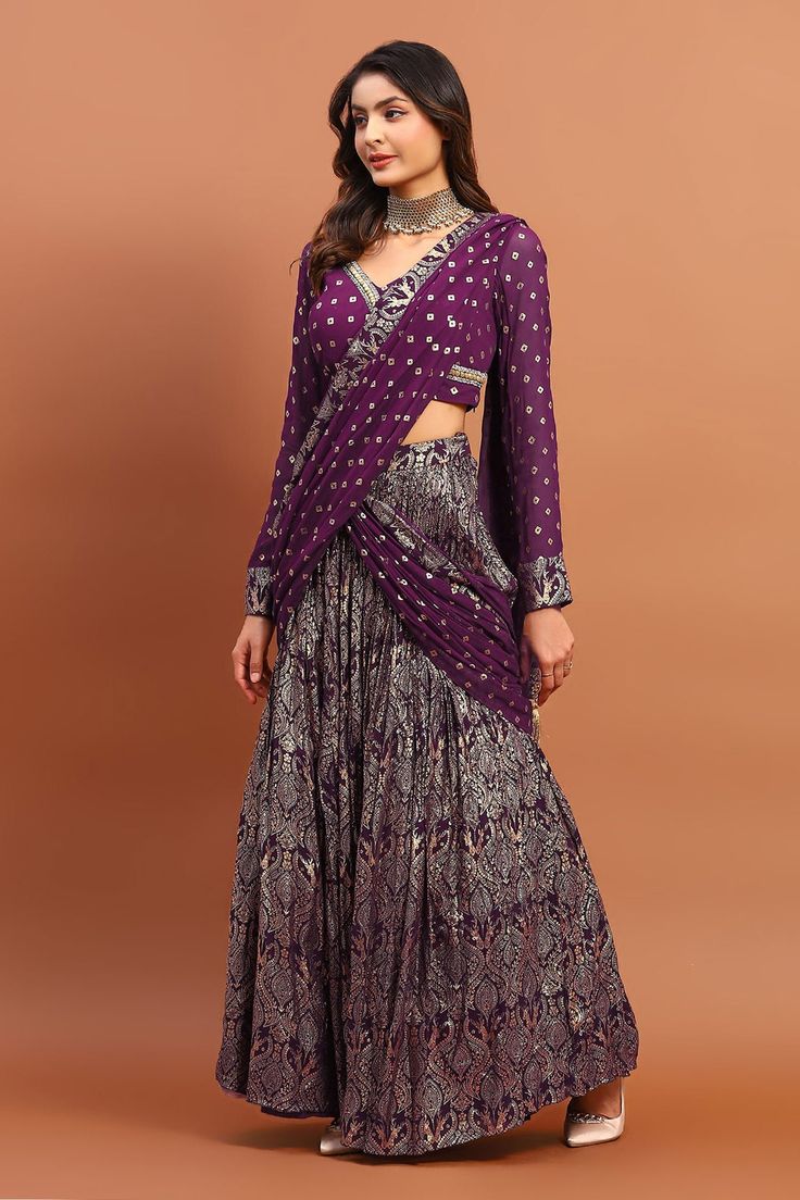 Purple georgette lehenga saree with all over vintage foil print and bandhani print attached pleated draped pallu. Paired with printed blouse with sequin and bead embroidered V neck.
Components: 2
Pattern: Printed and Hand Embroidered
Type Of Work: Bandhani, Foil Print, Bead and Sequin Work
Neckline: V Neck
Sleeve Type: Full Sleeves
Fabric: Georgette
Color: Purple
Other Details: 
Drop tasselled pallu
Pleated flare
Closure:
Saree: Side concealed zip
Blouse: Side concealed zip
Occasion: Wedding,Des Bandhani Lehenga, Saree Gowns, Dhoti Saree, Cotton Sarees Handloom, Bandhani Print, Printed Lehenga, Saree And Blouse, Georgette Lehenga, Full Sleeve Blouse