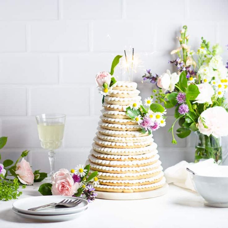 a white table topped with a cake covered in cookies next to flowers and wine glasses