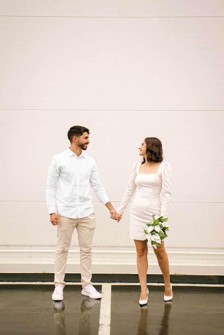 a man and woman holding hands while standing next to each other in front of a white wall