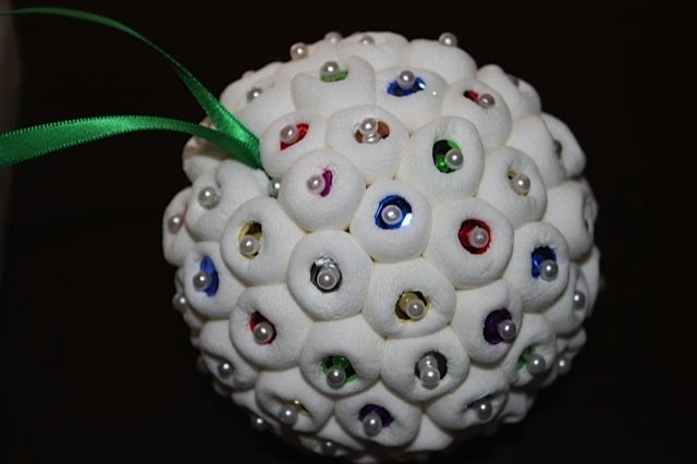 a white ornament with lots of colored stones on it and a green ribbon