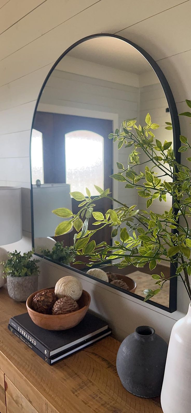 there is a mirror and some plants on the table in front of it with books