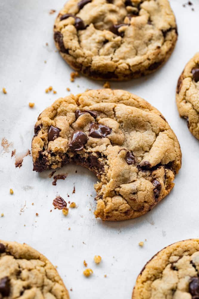 several chocolate chip cookies on a baking sheet with one broken in half and the other partially eaten