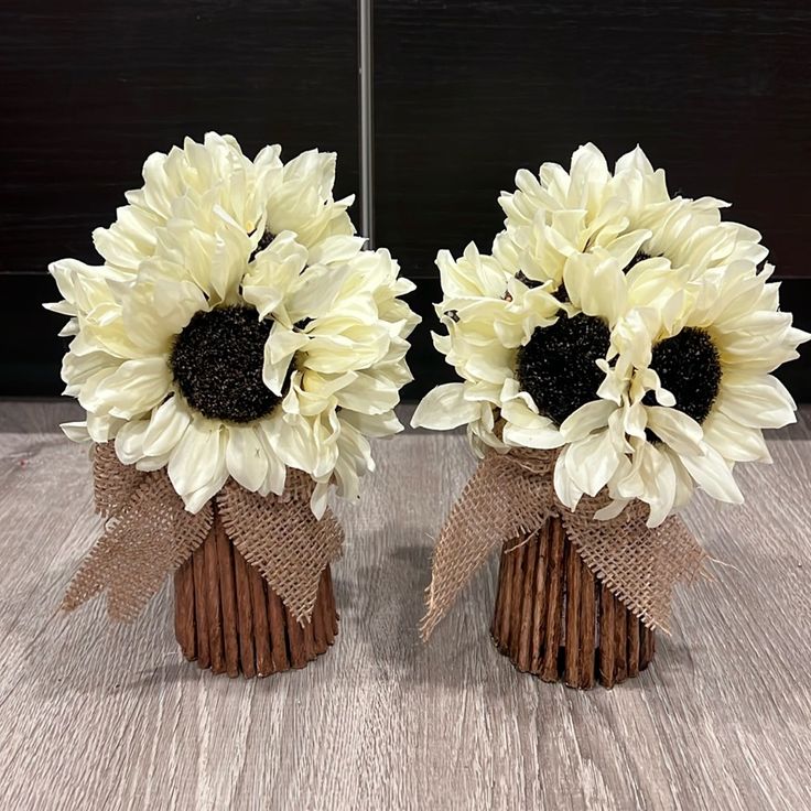 two vases with sunflowers are sitting on a table together, one is brown and the other is white