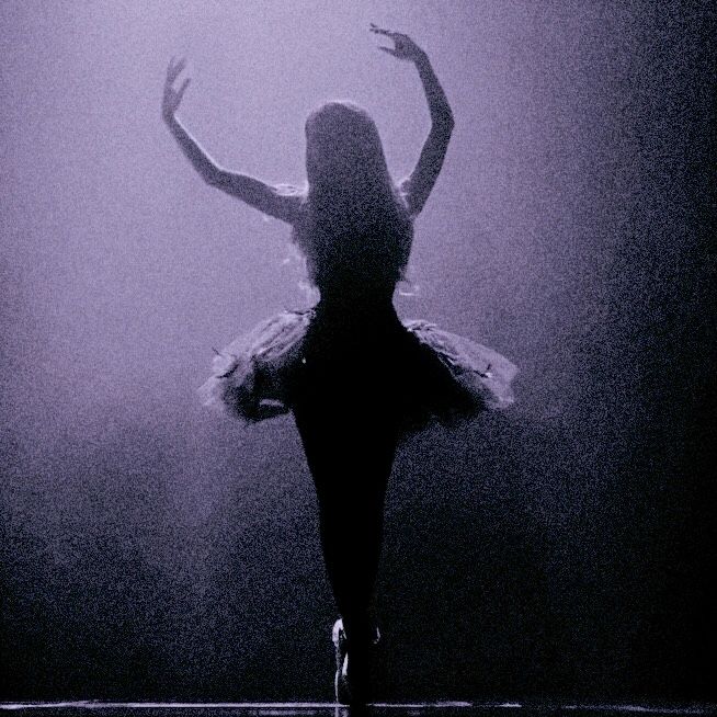 a ballerina is dancing in the dark with her arms spread out and hands outstretched