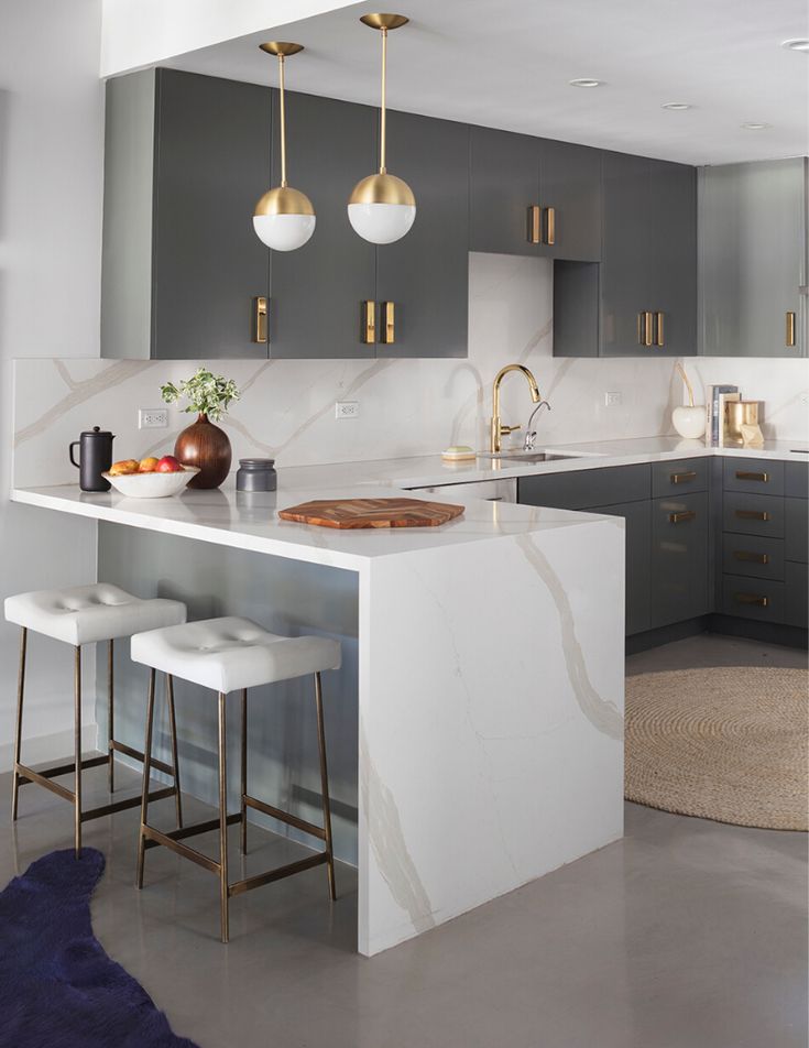 a modern kitchen with marble counter tops and gold pendant lights hanging from the ceiling over the island